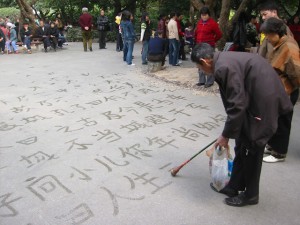 Elderly writing Chinese on pavement with water